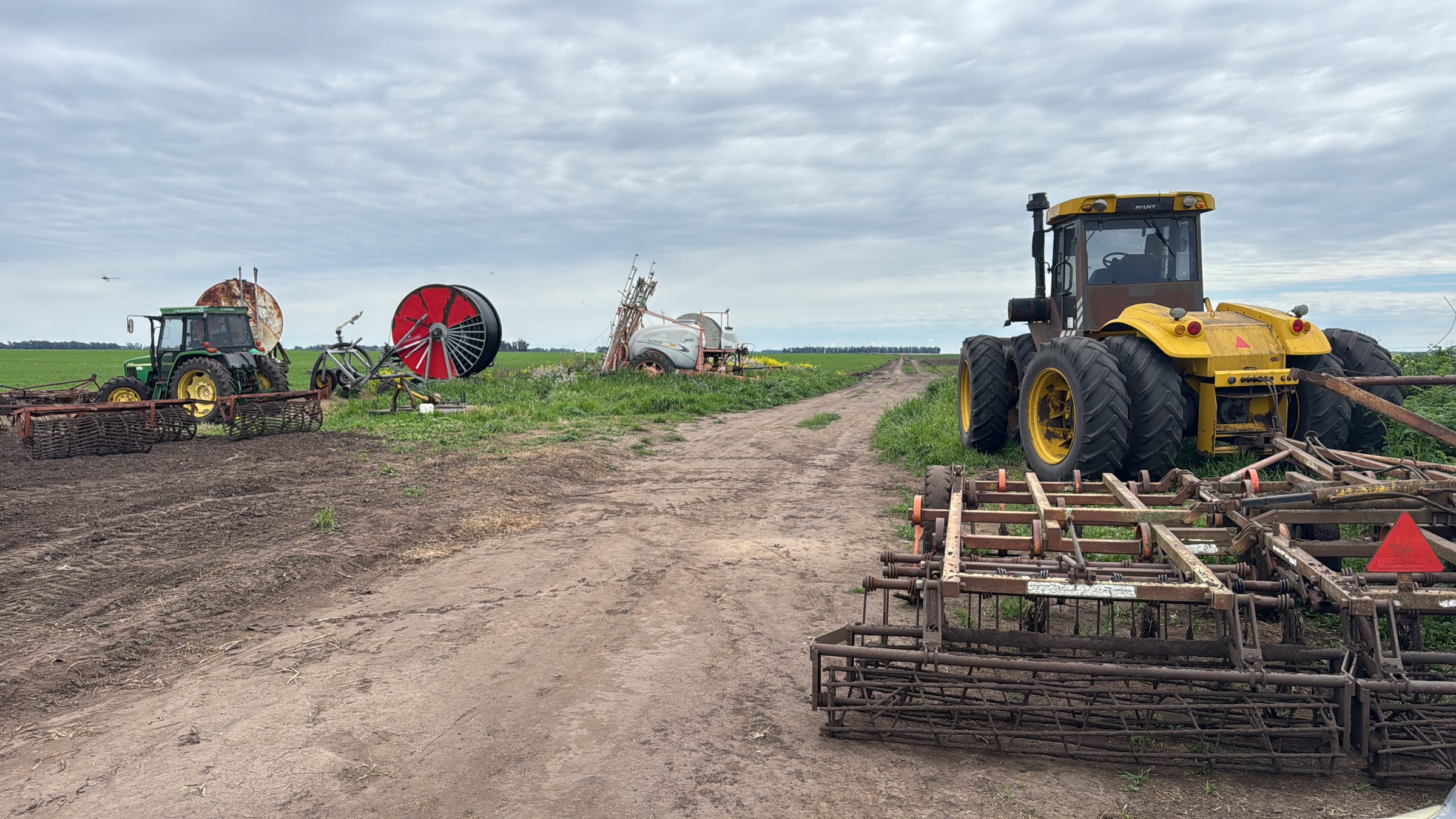 Tractores, rastra y pulverizadora en el campo bajo cielo nublado